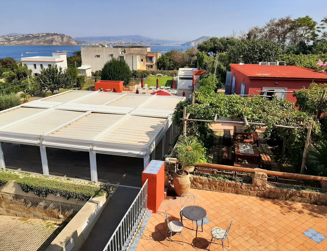 A Mediterranean property with red-roofed structures, terraced gardens, and a panoramic sea view overlooking a coastal bay.