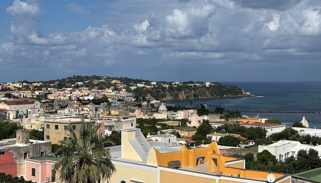 Panoramic coastal view of a colorful hillside town overlooking the Mediterranean Sea with white clouds in a blue sky.